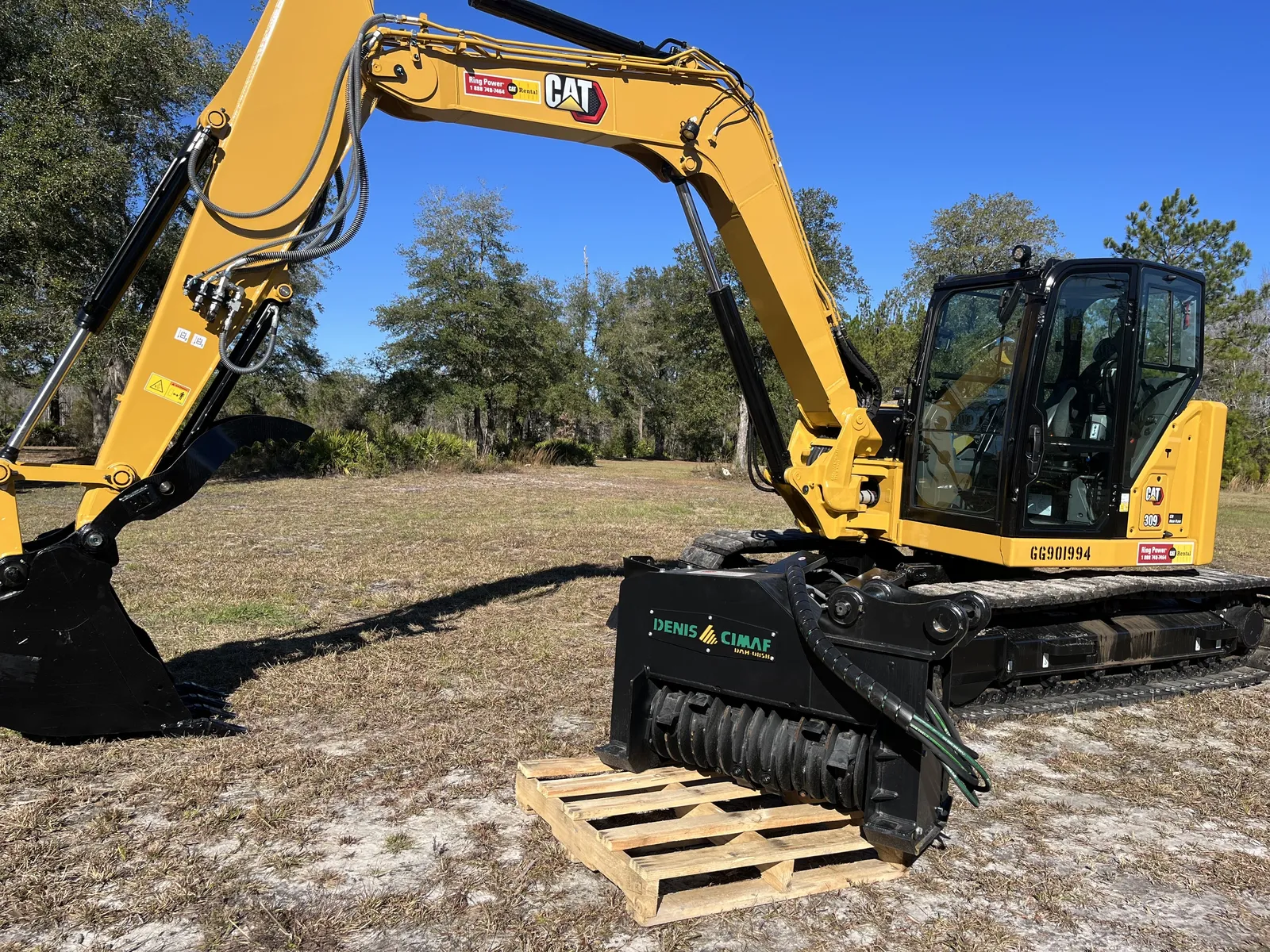 Our compact excavator beside its mulching head, ready to swap from the bucket to the mulcher