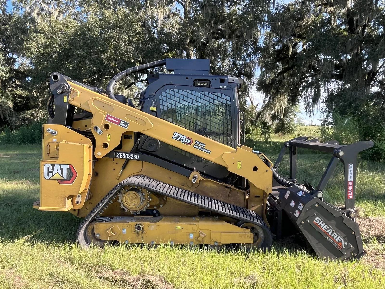 Our tracked skid steer with the forestry mulching head, parked on pasture under live oaks