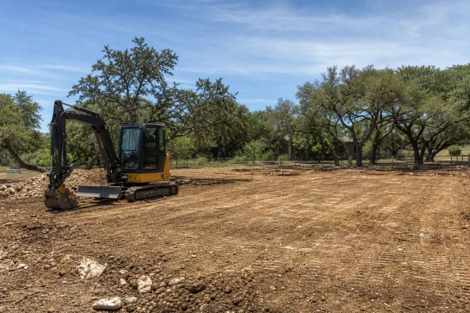Compact excavator sitting on freshly graded dirt pad during excavation work on rural acreage