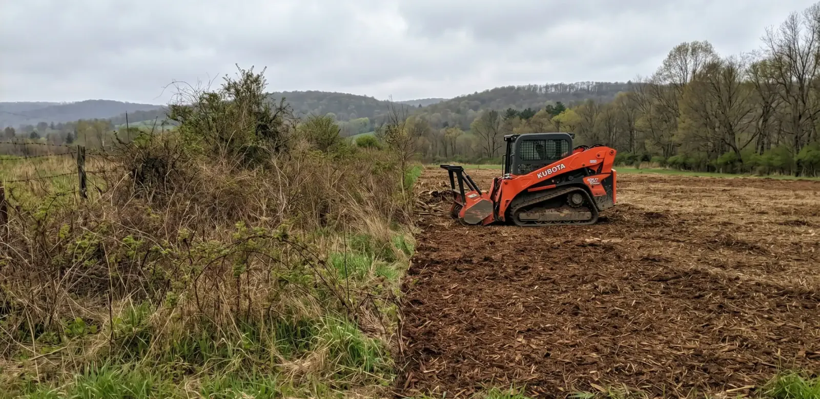 Track loader mulching an overgrown fence row of brush and vines on farm pasture