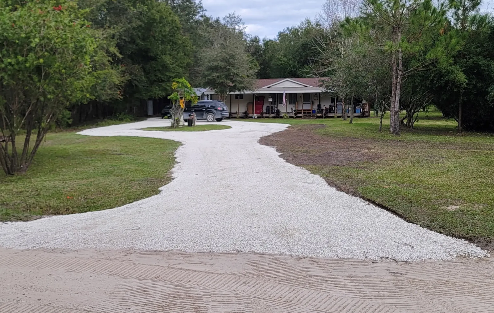 New limerock gravel driveway curving through shade trees toward a rural country home