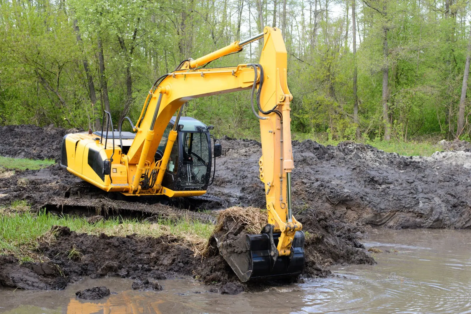 Excavator digging wet soil from a new pond basin during farm pond construction